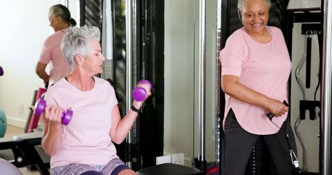 Senior lesbian couple exercising with weights in home gym