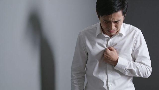 Asian man clutching chest grimacing from chest pain with dramatic shadow and copy space