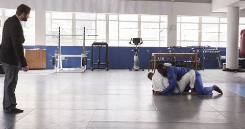 Coach Overseeing Grappling Students in Well-Equipped Gym