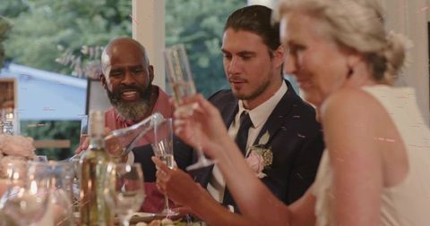 Groom and guests raising champagne flutes while elder guest pouring toast at garden reception