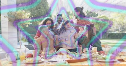 Friends Gathering on Backyard Patio Around Festive Dining Table with Neon Star Overlay