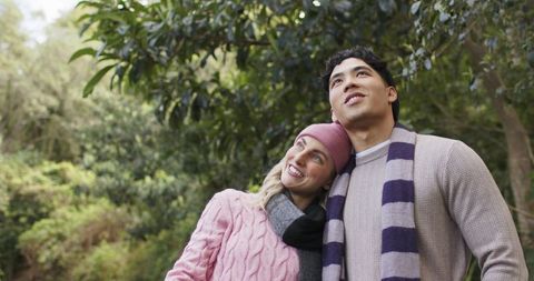 Diverse couple enjoying peaceful forest walk wearing cozy knit sweaters and scarves