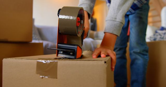 Person Sealing Cardboard Box with Tape Dispenser in Living Room - Download Free Stock Images Pikwizard.com