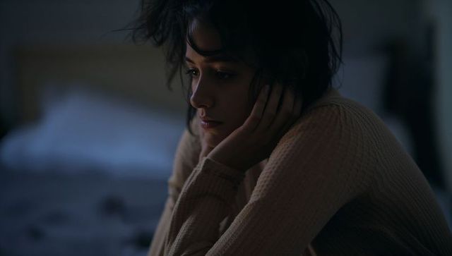 Moody bedroom portrait of young woman gazing thoughtful into warm light, nighttime intimacy