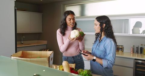 Women Unpacking Groceries in Modern Kitchen Analyzing Fresh Produce