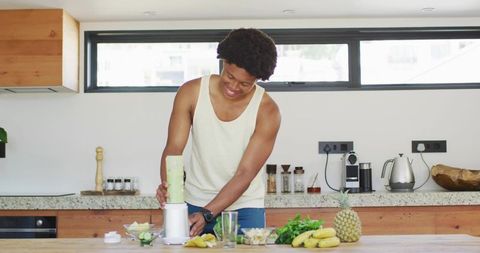 African American man blending green fruit smoothie on modern kitchen island, healthy lifestyle