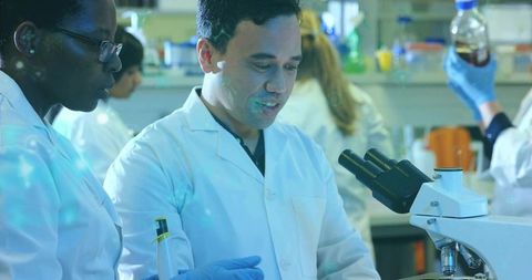Male researcher operating compound microscope, team collaborating, conducting lab research