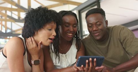 African american friends sharing smartphone moment in sunlit coworking space, smiling