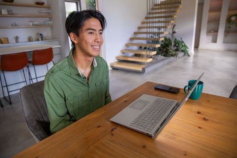 Young asian man working remotely in minimalist modern home workspace with laptop and mug