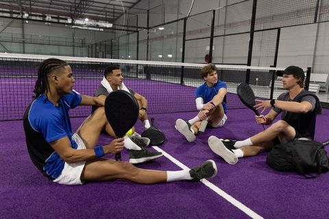 Four players sitting on purple court discussing strategy in paddle tennis training