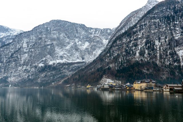 Hallstatt village, nestled by a tranquil lake with a backdrop of snowy mountains, offers a picturesque winter scene. This image captures the serene beauty of this Austrian village, mirroring in the clear lake. Ideal for tourism promotions, travel blogs, or seasonal greeting cards aiming to evoke a calm and beautiful destination.