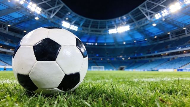 Close-up black-and-white soccer ball on grass under stadium floodlights with empty blue stands