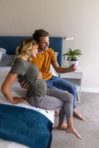 Expectant Couple Taking Selfie While Cradling Baby Bump in Cozy Bedroom