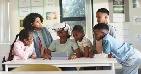 Diverse students exploring virtual reality headset at classroom table using tablet