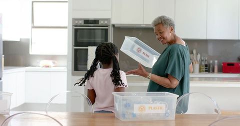 African grandmother teaching granddaughter recycling with labeled glass and plastic bins