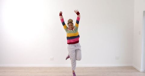 Joyful african american woman dancing indoors in colorful sweater