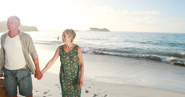 Elderly couple holding hands and walking along beach during sunset, representing senior lifestyle, love, and togetherness. Ideal for use in advertisements, websites, and articles related to retirement, relationships, and leisure activities.