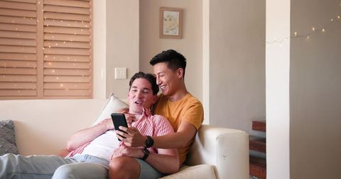 Happy Gay Couple Relaxing on Couch Looking at Smartphone