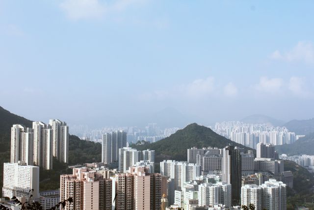 Cityscape featuring a densely populated urban region interspersed with high-rise buildings and distinct hilly landscape in the background, under a clear and bright sky. Ideal for themes related to urban living, real estate, city planning, and geographical contrast between natural and built environments.