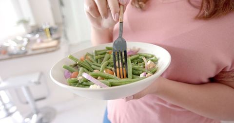 Healthy Eating Habits: Woman Enjoying Fresh Vegetable Salad in Modern Kitchen