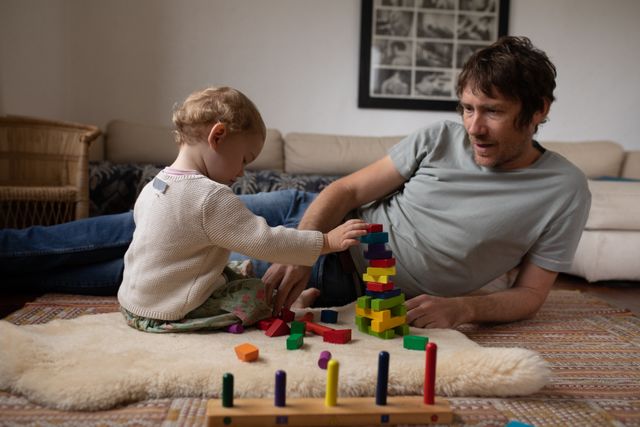 Front view of a young Caucasian father playing with his baby on a floor with colorful wooden building blocks.