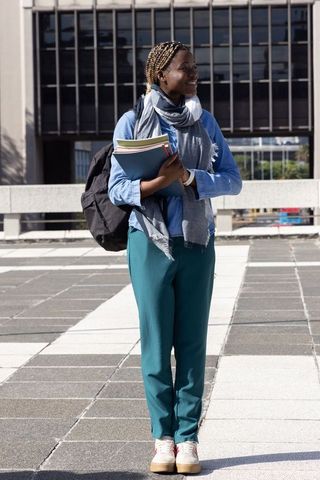 African american college student smiling and holding notebooks on urban campus plaza