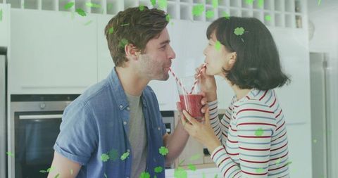 Couple sharing berry smoothie in bright modern kitchen leaning in for romantic sip