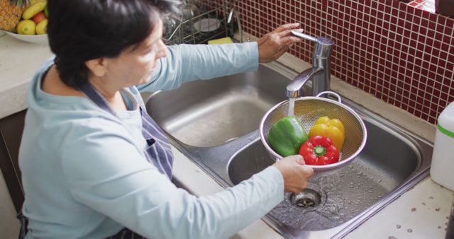 Asian senior woman wearing an apron washing vegetables in the sink at home. retirement lifestyle and living concept
