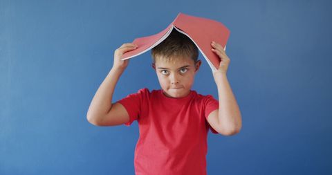 Thoughtful boy holding schoolbook against blue background