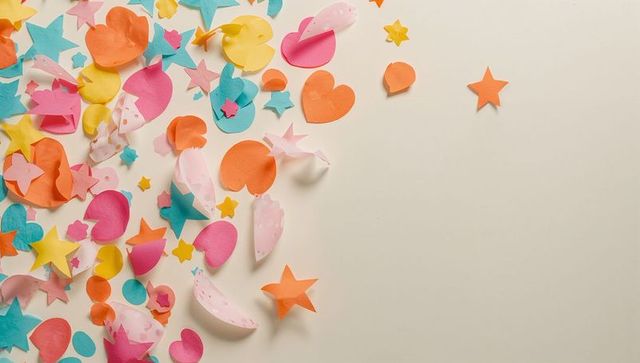 Colorful paper confetti hearts and stars scattering on cream flat lay with soft shadows