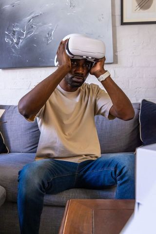 African man adjusting white vr headset while sitting on sofa in minimalist living room