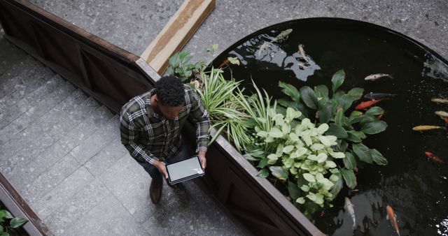 This portrays a businessman holding a tablet and studying a fountain area in an office lobby. Useful for themes of work-life balance, modern workspace design, concentration, and multitasking in a professional setting.