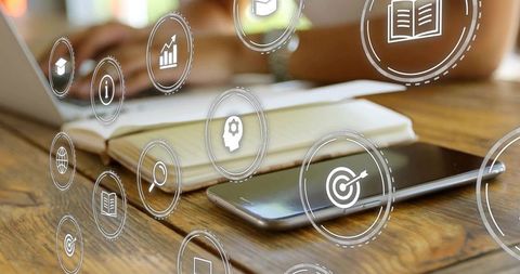 Smartphone resting on wood desk while typing laptop and e-learning icons floating
