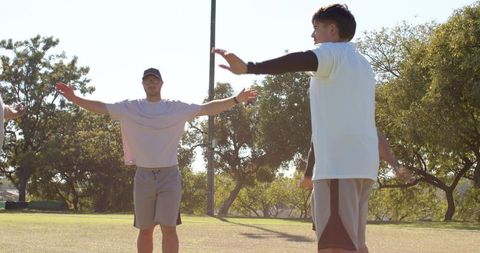 Diverse teammates stretching arms during warm-up on park sports field
