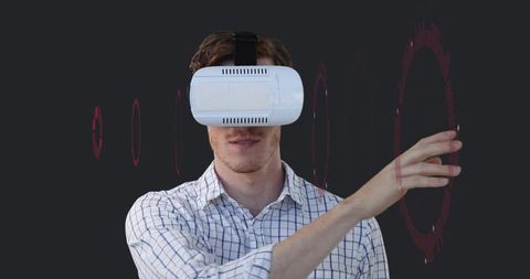 Young Man Wearing VR Headset Interacting with Virtual HUD Using Gesture Control on Dark Background