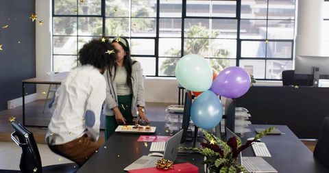 Colleagues celebrating birthday with cupcakes and balloons in bright open office