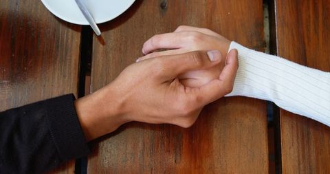 Close Up of Interracial Couple Holding Hands in Cafe