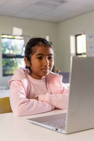 Indian schoolgirl learning on laptop in classroom wearing pink hoodie