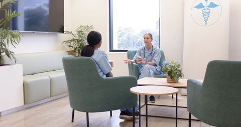 Nurses discussing break over coffee in modern medical lounge with stethoscope and greenery