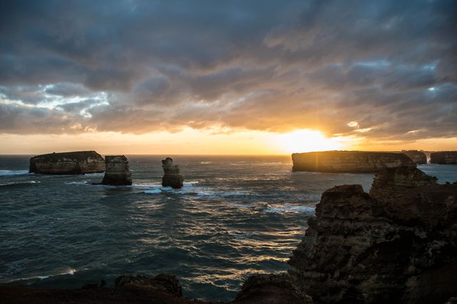 This image captures a stunning coastal landscape with ocean cliffs bathed in dramatic golden light at sunset. The sea stacks and crashing waves add visual interest and show the raw power of nature. Perfect for use in travel brochures, environmental campaigns, desktop wallpapers, or nature-focused websites to convey beauty, serenity, and the majesty of natural landscapes.