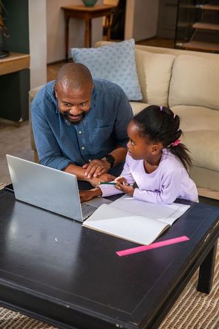 African american father helping daughter with homework on laptop, learning together
