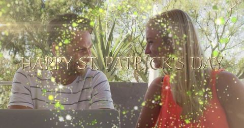 Happy St. Patrick's Day Couple Sharing Laptop on Sunlit Patio with Green Sparkle Bokeh