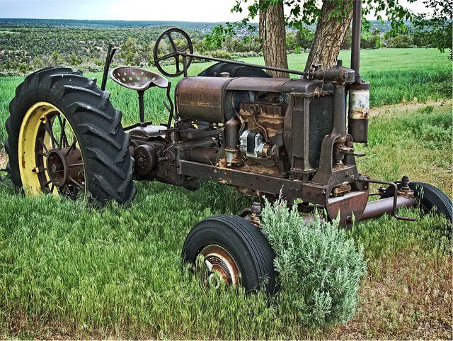 This image showcases an antique, rusty tractor sitting in an overgrown field with lush green surroundings. Ideal for use in articles about agricultural history, rural life, sustainable farming practices, or vintage machinery. It can also be used in advertisements and promotional material for farming equipment restoration services or events focused on farming heritage.