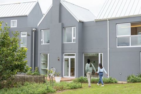 Couple walking toward modern gray house with glass doors and lush backyard garden