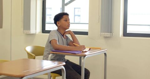 Focused Boy Studying at Classroom Desk with Pencil and Notebook