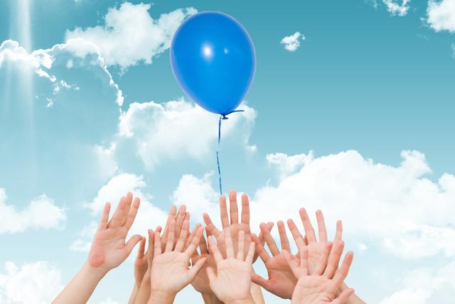 Hands of multiple people reaching towards a blue balloon floating in a bright, cloudy sky. This image symbolizes teamwork, aspiration, and unity. Ideal for use in motivational materials, team-building promotions, childhood memories, and celebration themes.