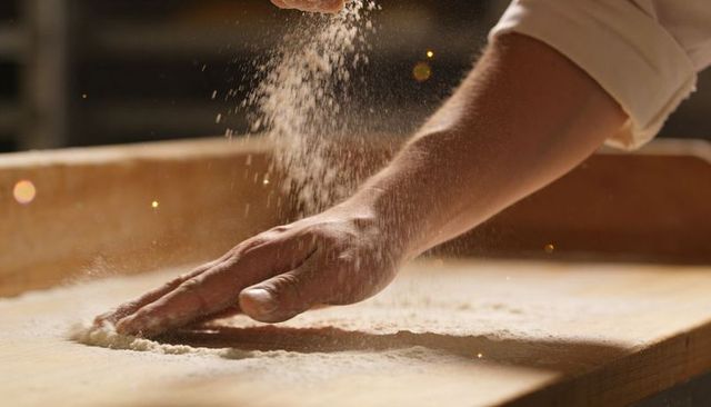 Baker dusting wooden board with flour for artisan dough preparation close-up