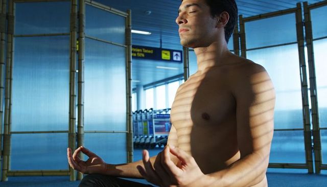 Shirtless man practicing airport meditation, sunlit mindfulness in terminal lounge