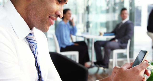 Businessman texting in modern office building with colleagues interacting in background - Download Free Stock Images Pikwizard.com