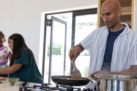 Multicultural family cooking in bright modern kitchen man stirring pan on gas cooktop
